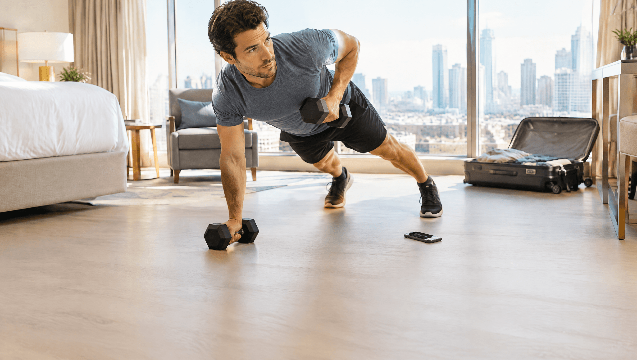 Hombre entrenando con mancuernas en la habitación de un hotel, con el móvil en el suelo